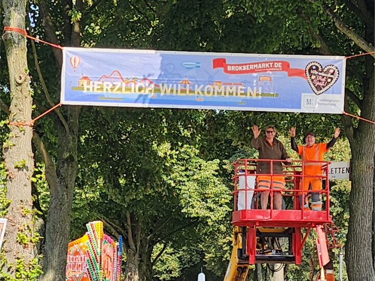 Zwei Männer stehen auf einer Hebebühne unter dem Eingangsbanner